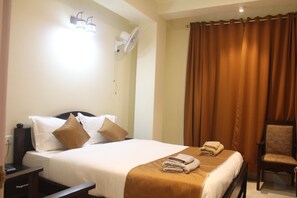 A hotel room with a bed, a chair, a desk, and a wall-mounted fan. - Vanagleda Guest House (Shillong)