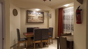 Un coin repas avec une table en bois et des chaises à revêtement gris, un ventilateur de plafond et un tableau accroché au mur.