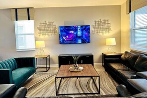 A modern living room with a flat-screen TV, two side tables with lamps, a coffee table, and a sofa.