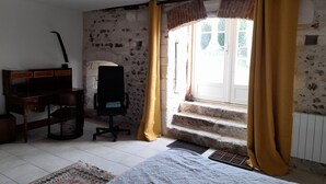 A bedroom with a bed, a desk, a chair, a radiator, and a window with curtains. - Harcourt priory (Harcourt)