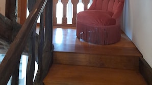 A staircase with a wooden handrail and a red upholstered chair at the bottom. - Harcourt priory (Harcourt)