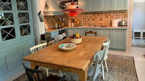 Une cuisine avec une table en bois, des chaises et un buffet bleu dont les portes sont en verre.