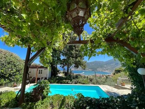 A pool surrounded by lush greenery and a view of a lake and mountains. - Romantic Lemonia Cottage with Private Pool & Sea View (Skopelos)
