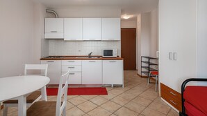 Une cuisine compacte avec des meubles blancs, un four à micro-ondes et un évier. On y trouve une table à manger avec des chaises et un tapis rouge.
