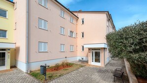 Un immeuble résidentiel à plusieurs étages doté d’une cour pavée, d’un banc et d’un petit espace jardin.