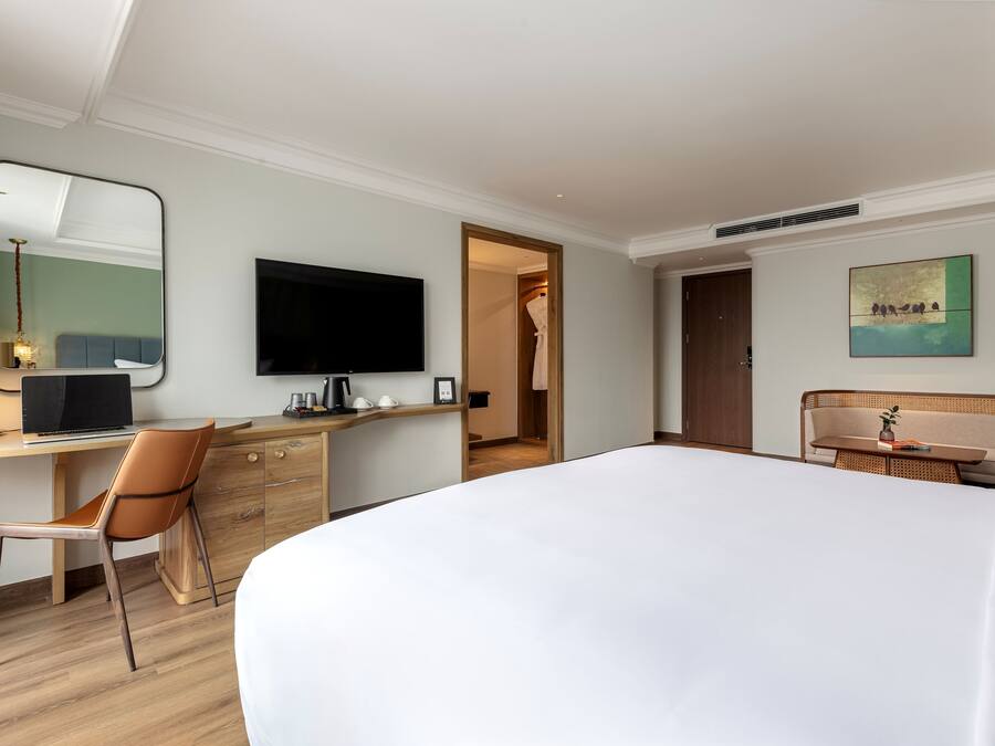 Une chambre d’hôtel avec un grand lit, un bureau avec une chaise, une télévision et un tableau au mur.