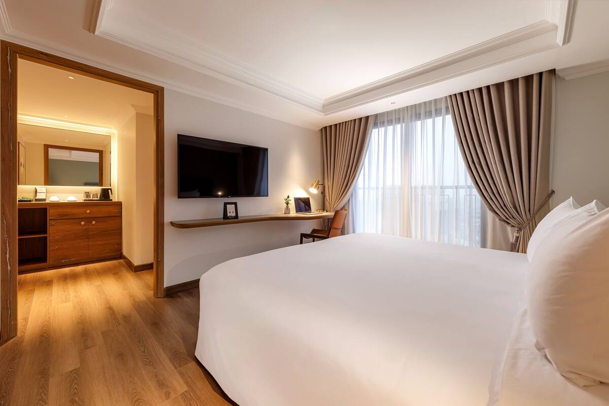 Une chambre d’hôtel avec un grand lit, un téléviseur fixé au mur, un bureau avec une lampe et une armoire en bois.