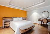 A hotel room with a large bed, a bedside table, a chair, a desk, and a mirror.