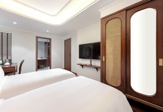 A hotel room with two beds, a television, a wooden wardrobe, and a mirror.