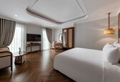 A modern hotel room with a large bed, a desk, a television, and a dining area.