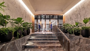 A marble staircase with potted plants on either side, leading to a glass door entrance.