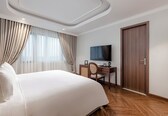A hotel room with a large bed, a desk with a chair, a television, and a wooden door.