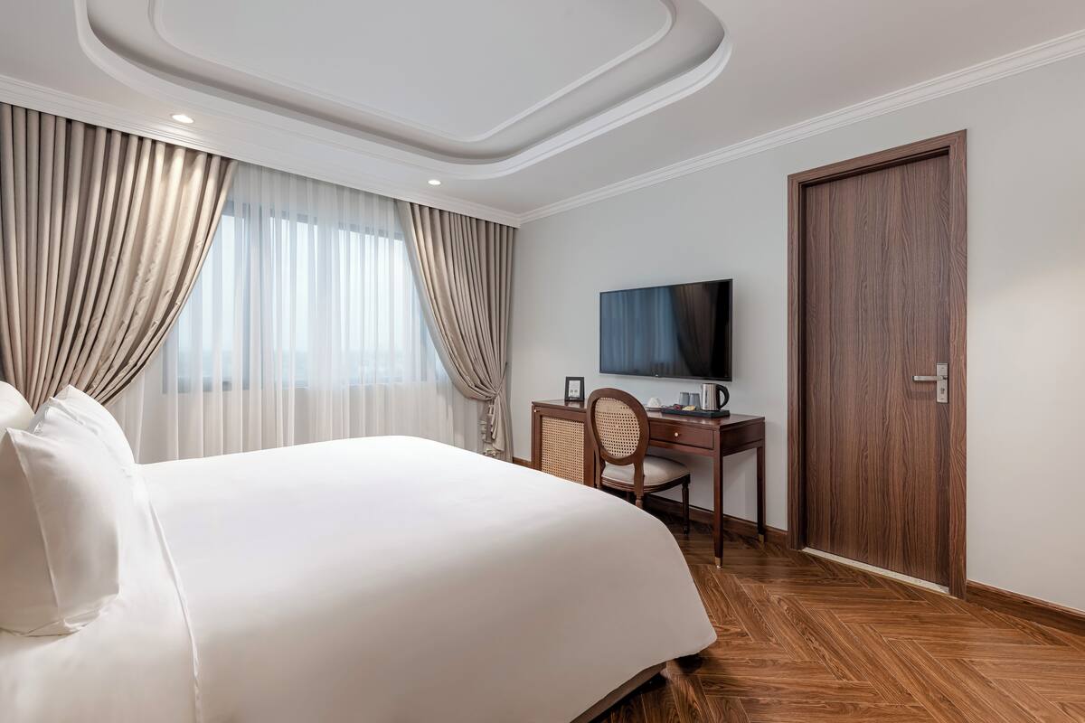 Une chambre d’hôtel avec un grand lit, un bureau avec une chaise, une télévision et une porte en bois.