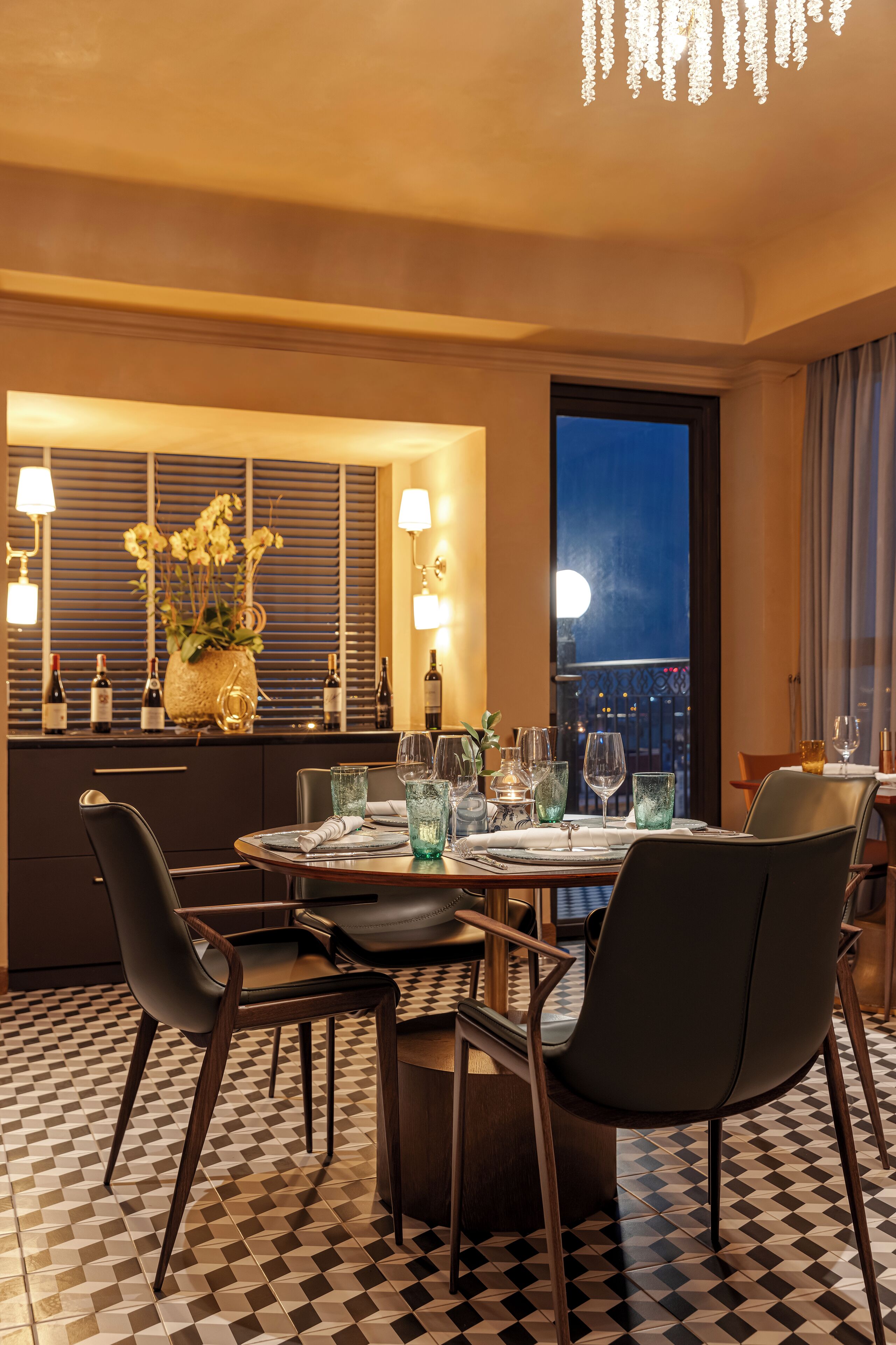 A dining area with a checkered floor, a round table set for four, and a view of the cityscape through a large window.