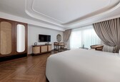 A hotel room with a large bed, wooden wardrobe, television, and a small table with chairs.