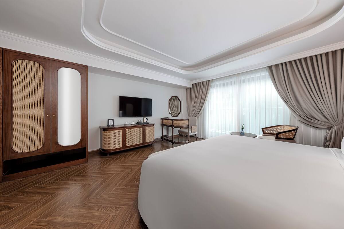 Une chambre d’hôtel avec un grand lit, une armoire en bois, une télévision et une petite table avec des chaises.