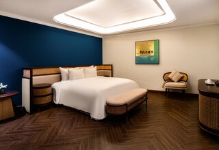 A bedroom with a large bed, a bedside table, a chair, a small table, and a wall-mounted TV.