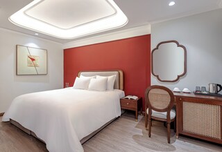 A hotel room with a large bed, a desk with a chair, a nightstand, a mirror, and a framed artwork on the wall.