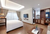 A hotel room with a large bed, a TV, a wooden wardrobe, and a small table with a book and glasses.