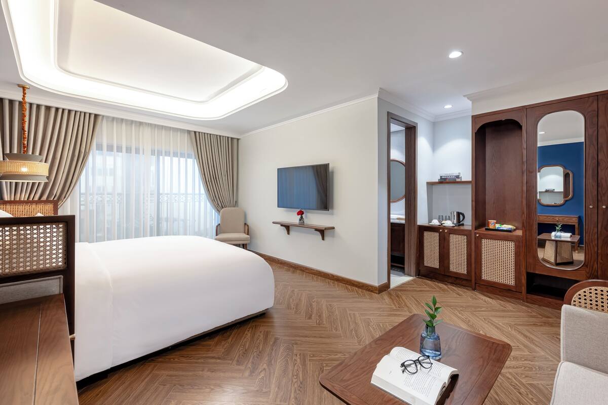 Une chambre d’hôtel avec un grand lit, une télévision, une armoire en bois et une petite table sur laquelle se trouvent un livre et des lunettes.