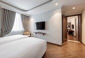 A hotel room with two beds, a TV mounted on the wall, a wooden floor, and a view of the hallway.