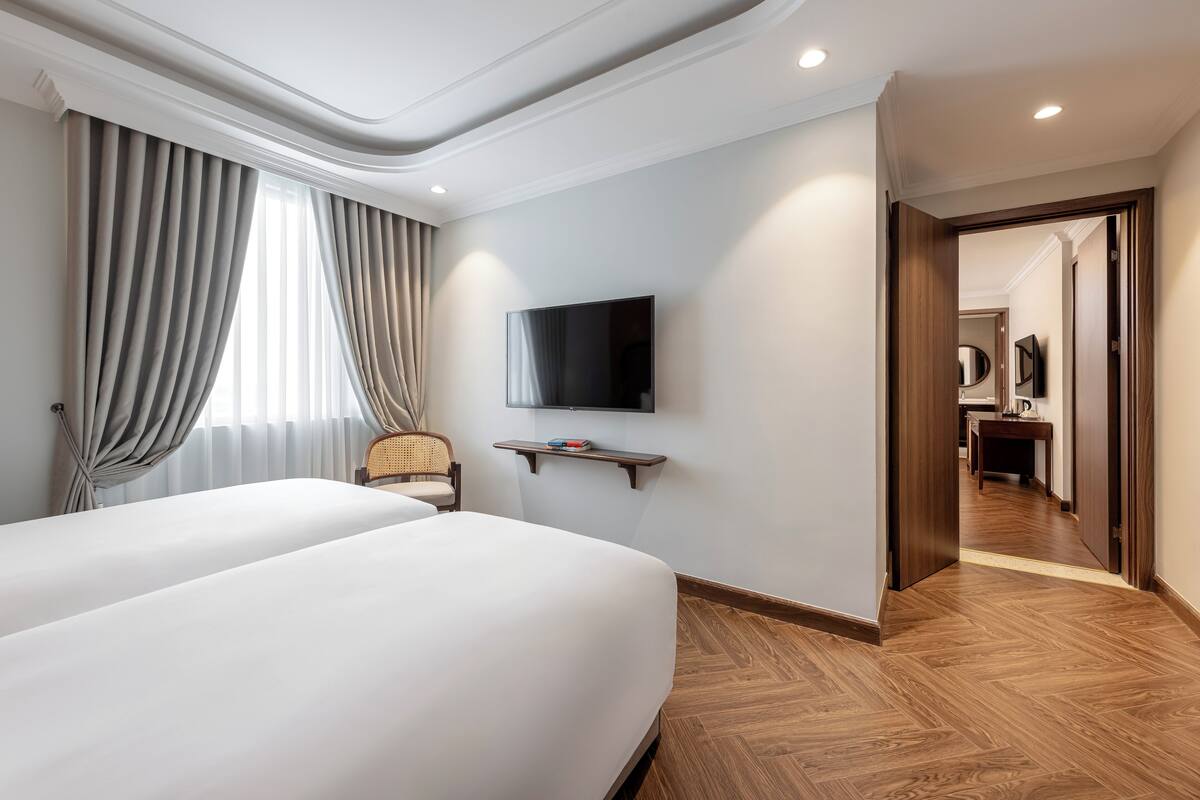 Une chambre d’hôtel avec deux lits, un téléviseur fixé au mur, un plancher en bois et une vue sur le couloir.
