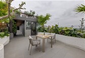 An outdoor patio with a table and chairs, surrounded by lush greenery and a view of the sea.