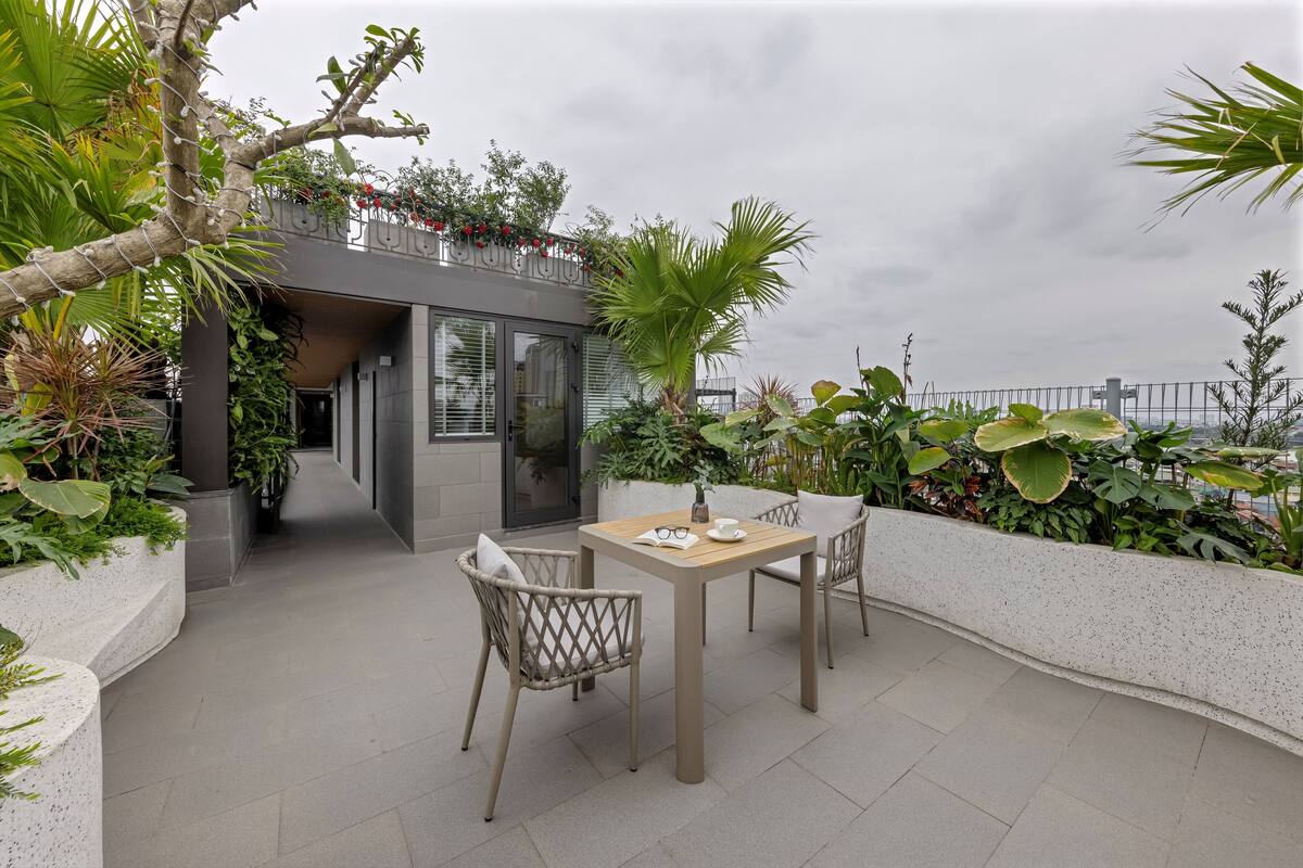 Une terrasse extérieure avec une table et des chaises, entourée d’une végétation luxuriante et offrant une vue sur la mer.