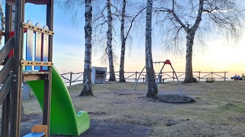 Une aire de jeux avec un toboggan, des balançoires et un espace clos, agrémenté d’arbres.