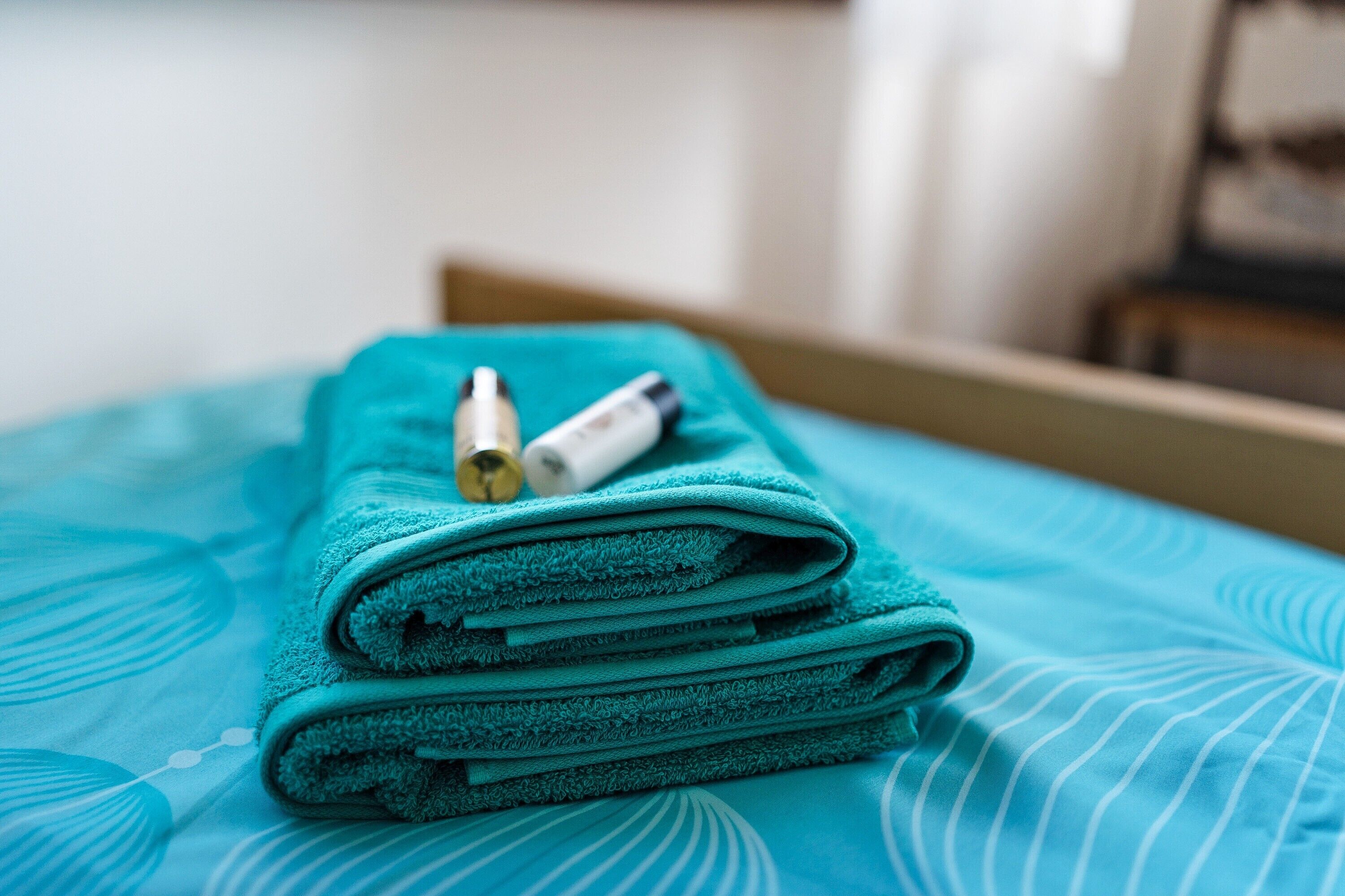 A neatly folded teal towel on a bed with a patterned bedspread.