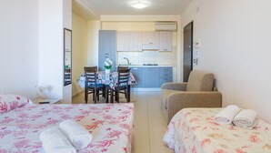 Habitació d'hotel amb dos llits, una taula de dinar amb cadires, una cuineta i un sofà.