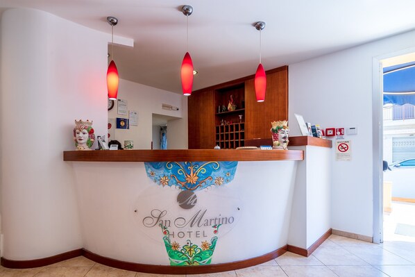 A reception desk at San Martino Hotel with a decorative emblem, a clock, and a 'No Smoking' sign.