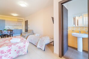 Une chambre avec deux lits, une salle de bain avec un lavabo et un coin cuisine.