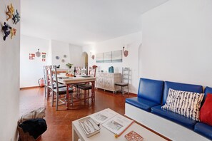 A living room with a blue sofa, a dining area with a table and chairs, and a kitchen area with cabinets and a countertop.