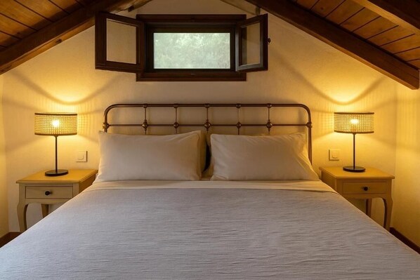 A bedroom with a sloped ceiling, a bed with white linens, two bedside tables with lamps, and a window above the bed. - Romantic Pergamonto Cottage with private Pool & SeaView (Skopelos)