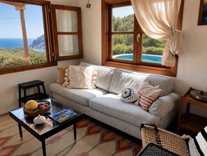 A cozy living room with a sofa, a coffee table with a magazine, and a view of a pool and greenery.