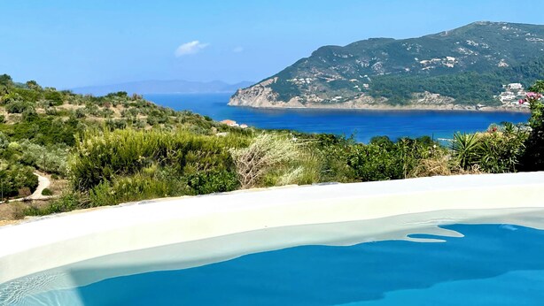 Una piscina con vista despejada al mar y un paisaje montañoso de fondo.