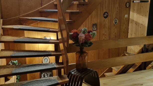 Un escalier en bois avec un vase de fleurs posé sur la plateforme.