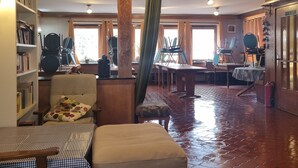 Une pièce spacieuse avec un plafond haut, un plancher en bois et une colonne centrale ornée de motifs de vigne. On y trouve plusieurs chaises et une table, ainsi qu’une bibliothèque remplie de livres.