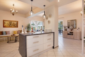 Een moderne keuken met een centraal eiland, hanglampen en een eethoek met een bank en tafel.