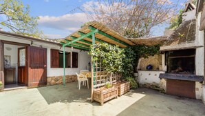 Eine rustikale Terrasse im Freien mit einer Holz-Pergola, einer Steinmauer und einem Backofen aus Ziegeln.