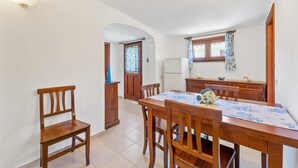 Ein Essbereich mit Holztisch und -stühlen, im Hintergrund eine Küche und eine weiße Wand mit einer Leuchte.