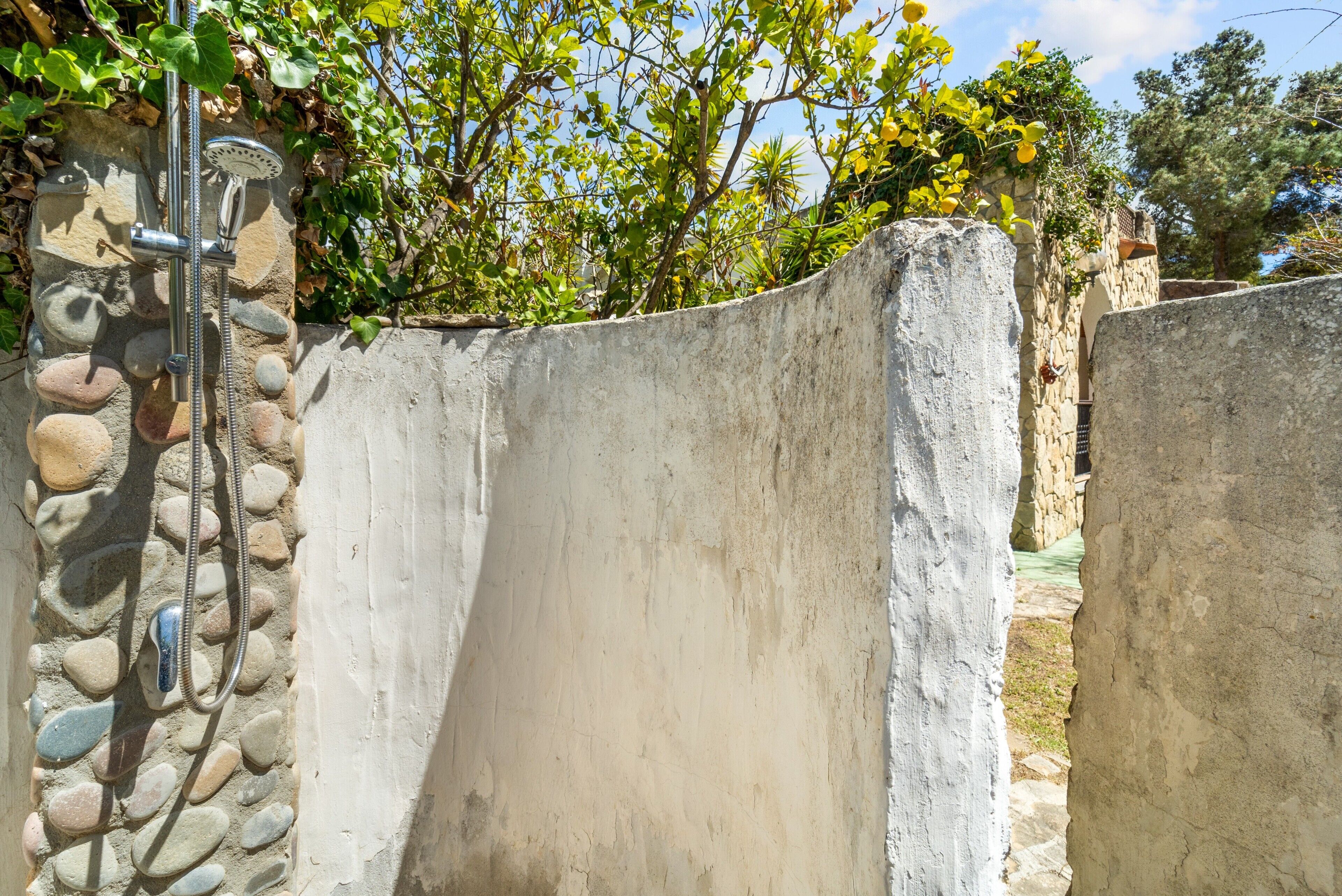 Un muro in cemento con una doccetta, un muro di pietra con ciottoli e vegetazione sullo sfondo.