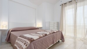 Ein Schlafzimmer mit Bett, Nachttischlampen, einem Schminktisch und durchsichtigen Vorhängen.