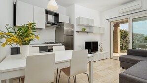 Eine moderne Küche mit weißen Schränken, ein Essbereich mit weißem Tisch und Stühlen sowie ein graues Sofa.