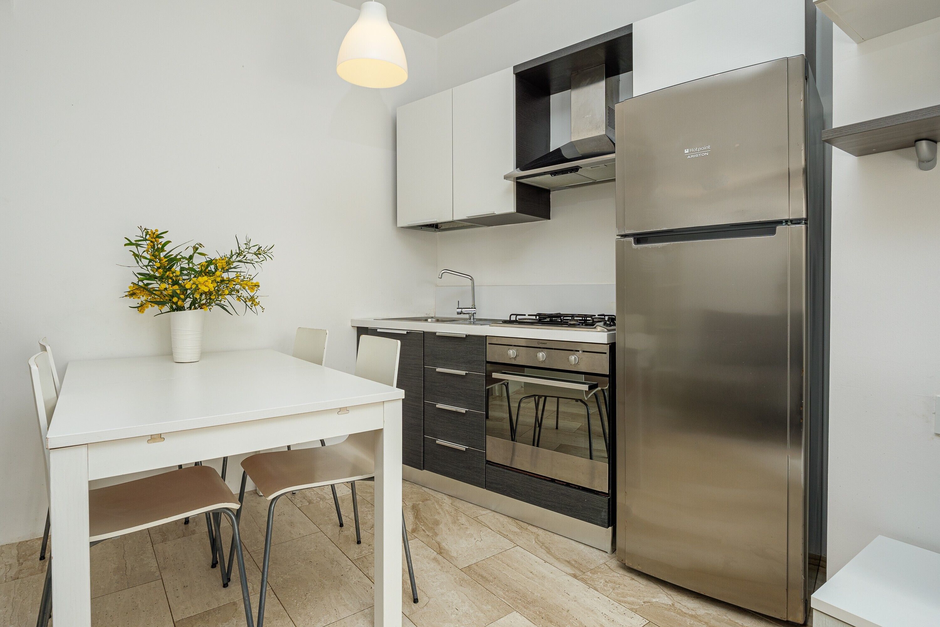 A modern kitchen with a white table, chairs, a stainless steel refrigerator, and a gas stove.