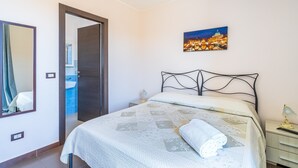 Un dormitorio con cama, mesita de noche, lámpara, un cuadro, espejo y una puerta que da al baño.