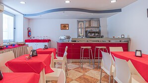Un restaurante con mesas y sillas rojas, una zona de cocina y un ventanal que proporciona luz natural.