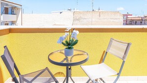 Una pequeña mesa redonda con una planta en maceta, dos sillas de malla y una pared amarilla.