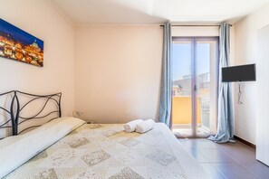 A bedroom with a bed, a painting, a TV, and a balcony with curtains.